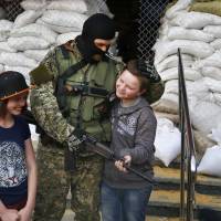An armed Pro-Russian militant poses for a photo with local children next to barricades in front of the Slovyansk City Hall in eastern Ukraine on Monday. | AP