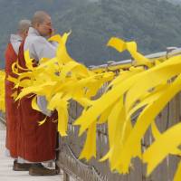 A Buddhist nun wipes her tears after attending a service as yellow ribbons are displayed as a sign of hope for the safe return of missing passengers of the sunken ferry Sewol at a port in Jindo, South Korea, on Saturday. | AP