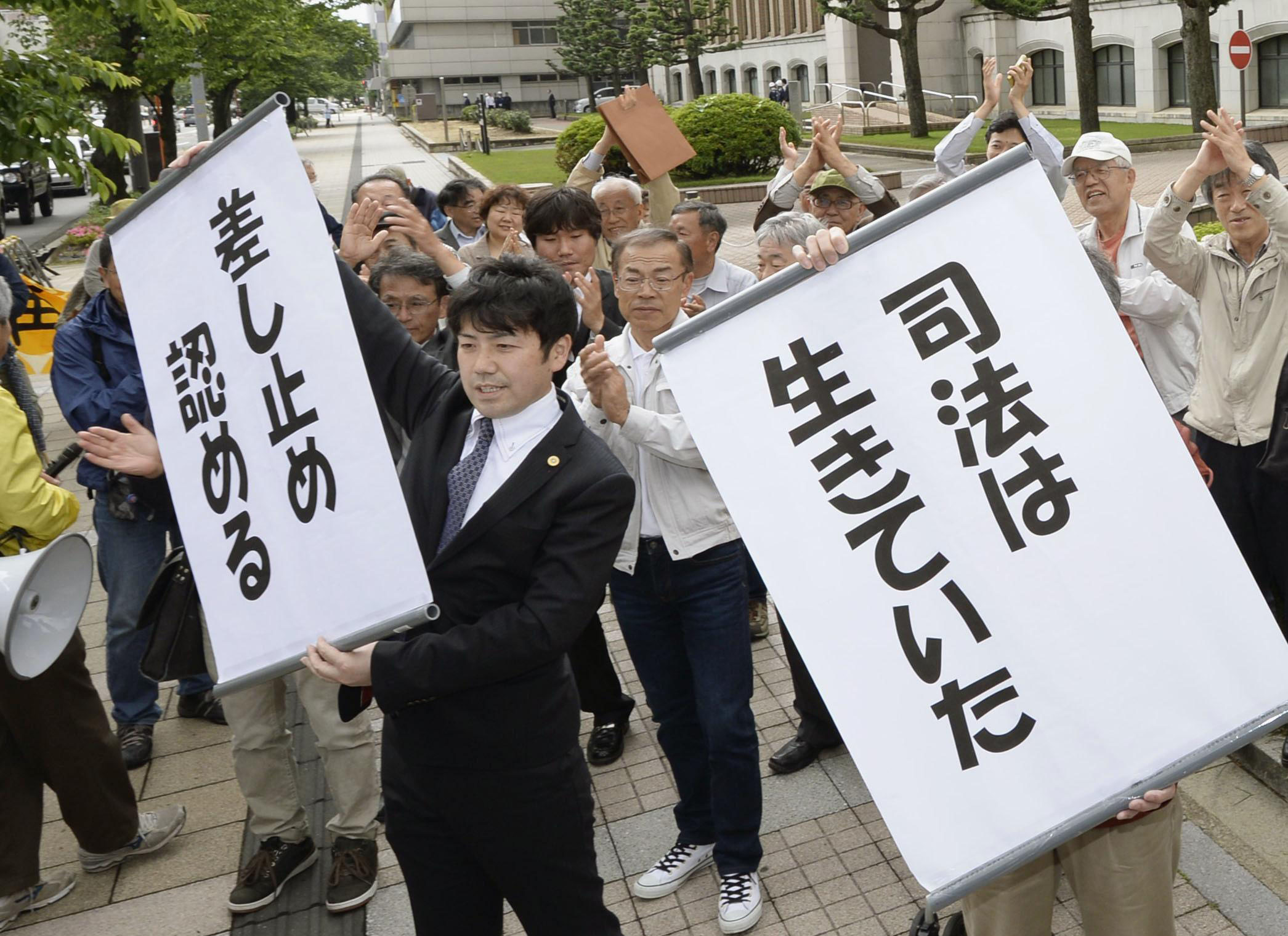 Lawyers hold signs reading 'justice is alive' and 'suspension has been ordered' at the Fukui District Court on Wednesday. | KYODO