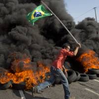 A member of the Homeless Workers Movement carries a Brazilian flag past burning tires during a May 15 protest against the money spent on the World Cup near Sao Paulo\'s Itaquerao stadium, which will host the soccer tournament\'s first match. | AP