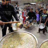 Palestinian refugees living at the Yarmouk camp, outside Damascus, line up to receive food rations on April 19. | REUTERS