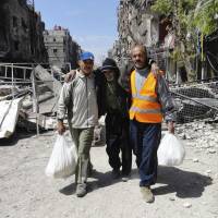 Palestinians living in the Yarmouk refugee camp outside Damascus help an elderly man as U.N. food aid is distributed on April 24. | REUTERS