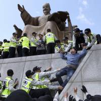 Policemen detain university students on a statue of King Sejong the Great during a protest in central Seoul on Thursday demanding President Park Geun-hye resign over the Sewol ferry disaster. | REUTERS