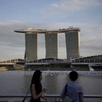 People stroll along the waterfront near the Marina Bay Sands hotel and casino in Singapore last December. Prime Minister Shinzo Abe plans to visit a casino and resort complex in the city-state later this month to gauge the economic effects of legalizing casinos in Japan. | BLOOMBERG