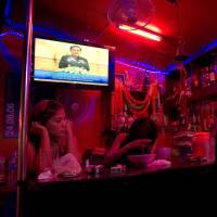 Thai Army chief Gen. Prayuth Chan-ocha (top left) makes a speech on television as workers wait for customers in a red light district of Bangkok on Friday. | AFP-JIJI