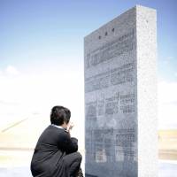 A woman cries in front of a stone memorial inscribed with the names of people claimed by the March 2011 tsunami in Iwanuma, Miyagi Prefecture, on Saturday. The memorial, erected in a park made from rubble left by the waves, was unveiled the same day. KYODO | KYODO