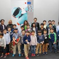 People pose against the backdrop of a large poster of a robot at an event on April 13 in Tokyo. | HABATAKI PROJECT BY SHINTAKUJYUKU