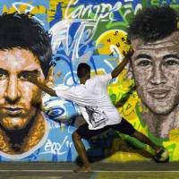 Residents of a favela in Rio de Janeiro play street soccer in front of a mural of Argentine national team lynchpin Lionel Messi (left) and Brazilian star Neymar. The FIFA World Cup kicks off Thursday in Brazil. | AFP-JIJI