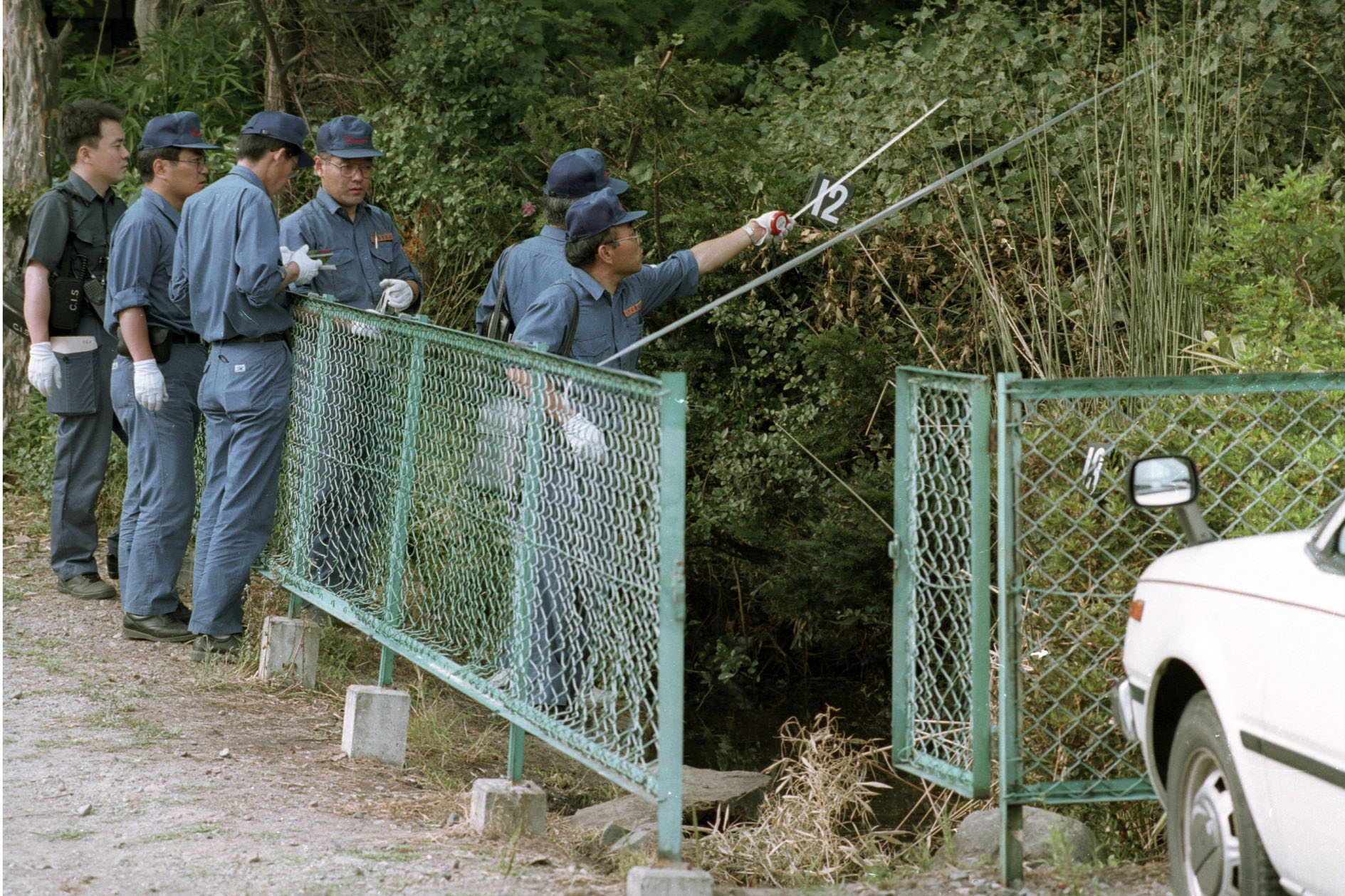 Investigators examine foliage surrounding a fish pond in Matsumoto, Nagano Prefecture, in June 1994 after sarin was detected in the area. | KYODO