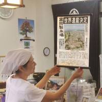 An employee at a shop near the Tomioka Silk Mill in Gunma Prefecture on Sunday displays a special edition of the daily Jomo Shimbun made of silk. | JOMO SHIMBUN/KYODO