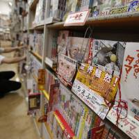 \"Ichi Efu\" (second from right), a manga about workers at the heavily damaged Fukushima No. 1 nuclear power plant, is seen on a bookshelf as a staffer rearranges comics at a bookstore in Tokyo on June 23. | REUTERS