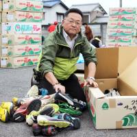 Toshio Sugiyama, head of a nonprofit group that donates used shoes to children in Cote d\'Ivoire, sorts through a pile of athletic shoes in April. He said the group will cheer for both Japan and Cote d\'Ivoire when the two teams meet in the World Cup in Brazil this weekend. | KYODO