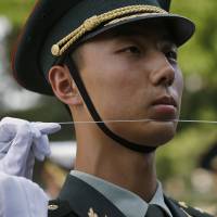 A Chinese People\'s Liberation Army soldier uses a string to ensure that soldiers, making up an honor guard, stand in a straight line before a ceremony in Beijing on June 12. | REUTERS