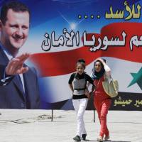 A pair of girls walk in front of a campaign billboard for Syrian leader Bashar Assad, who was expected to dominate Tuesday\'s presidential election. This billboard bears the slogan \"Yes for Assad . . . Yes for a secure Syria.\" | AFP-JIJI