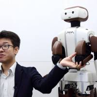 Wataru Yoshizaki, chief robot officer of Asratec Corp., speaks Tuesday next to the company\'s humanoid robot, Asra C1, in Tokyo. | BLOOMBERG