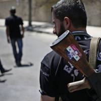 A Syrian soldier carrying an AK-47 with a sticker of Syrian President Bashar Assad and the Arabic words reading \"Syria is fine\" stands guard at a checkpoint in Damascus last Aug. 21. | AP