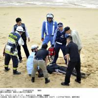 Police officers surround Yasuyuki Okuma, who was found lying on a beach in the city of Fukuoka on Monday morning after escaping from a hospital where he had been held for psychiatric evaluations earlier in the day. | KYODO