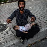 A Syrian refugee begs in the street with a baby lying on his lap in Istanbul on Thursday. The Syrian regime warned the U.N. Security Council in a letter drafted Wednesday that delivering humanitarian aid across its borders into rebel-held areas without its consent would amount to an attack. | AFP-JIJI