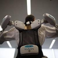 An employee of ActiveLink Co. conducts a demonstration with the ARM01 Raku Vest, a robotic exoskeleton jointly developed with Kubota Corp. to help farmers and construction workers, in Tokyo on Monday. | REUTERS