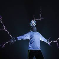 A performer with China\'s Thunderbolt Craziness rock band balances a soccer ball on his head as electricity discharges from Tesla coils below him. He is wearing a metal suit to protect him from the one million volt charge. The stunt, performed at a concert Thursday in China\'s Fujian province, marked the kickoff of the 2014 World Cup in Brazil. | REUTERS