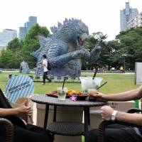 A couple sit a safe distance from Godzilla, or that is a replica of  Godzilla currently terrorizing Tokyo Midtown’s Midpark in Roppongi.  | YOSHIAKI MIURA