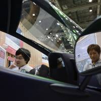 Visitors look at a Toyota i-ROAD electric personal mobility vehicle at the ITS World Congress in Tokyo last October. | BLOOMBERG