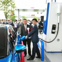 Chihiro Tobe, director of the Hydrogen and Fuel Cell Promotion Office at the Natural Resources and Energy Agency, charges a fuel-cell car as Iwatani Corp. President Masao Nomura watches at a new hydrogen filling station in Amagasaki, Hyogo Prefecture, on Monday. | KYODO