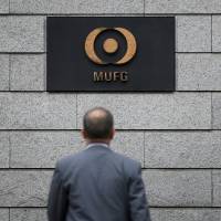 A man walks toward signs for Mitsubishi UFJ Financial Group Inc. outside its headquarters in Tokyo in May. | BLOOMBERG
