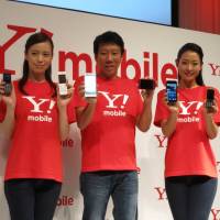 Flanked by models, Ymobile Corp. President Eric Gan shows off the fledgling company\'s first smartphones at a news conference in Tokyo on Thursday. | KAZUAKI NAGATA