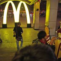 A Chinese man poses for photos with Ronald McDonald, the mascot for fast food restaurant McDonald\'s, outside one of its branches at a train station in Shenyang, China, in May 2011. McDonald\'s and KFC in China faced a new food safety scare Monday, after a Shanghai television station reported a supplier sold them expired beef and chicken. | AP