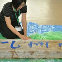 An official from the disaster-hit village of Tanohata in Iwate Prefecture touches a signboard that was swept away in the March 11, 2011, tsunami. The sign was returned to the village on Friday. | KYODO