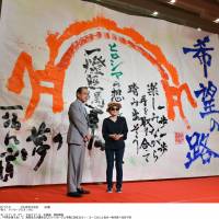 Artist Yoko Ono and Hiroshima Mayor Kazumi Matsui stand before a 4-meter-long, 6-meter-wide sheet with messages of peace written by local high school students in the city of Hiroshima on Wednesday, one week before the 69th anniversary of the atomic bombing. | KYODO