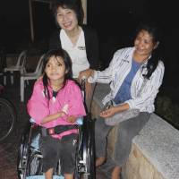 First set of wheels: Michiyo Yoshida (standing) delivers a used wheelchair to a child in Cebu, central Philippines, in January, so she can start going to school. | TAIZO YOSHIDA