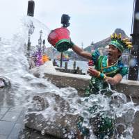 A Tokyo DisneySea cast member (right) throws water toward guests during a special summer attraction called \"Minnie\'s Tropical Splash\" at Tokyo DisneySea in Urayasu, Chiba Prefecture, on Wednesday. | AFP-JIJI