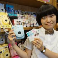 An employee at the Fujifilm camera and photo-print store in Tokyo’s trendy Harajuku district poses with a Cheki instant camera on July 28. Instant camera gets mojo back with cute focus, Korean push