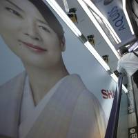 A shopper standing on an escalator rides past advertisements for Sharp Corp.\'s Aquos television at an electronics shop in Tokyo on Friday. | REUTERS
