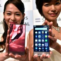 Models display new Sharp smartphones in Tokyo on Monday. Mobile communications giant SoftBank will start selling the Aquos Crystal (right) in Japan on Aug. 29, while subsidiary Sprint will launch it in the U.S. | AFP-JIJI