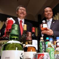 Nobutada Saji (left), chairman and chief executive officer of Suntory Holdings Ltd., and Takeshi Niinami, incoming president, show off some of the company\'s products during a news conference in Tokyo on July 1. | BLOOMBERG