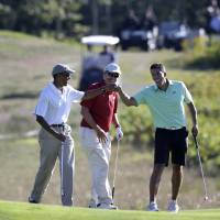 President Barack Obama bumps fists with Cyrus Walker, cousin of White House senior adviser Valerie Jarrett, as Glenn Hutchins looks on while golfing Thursday at Vineyard Golf Club in Edgartown on the Massachusetts island of Martha’s Vineyard. Obama taking less vacation, but too much for some