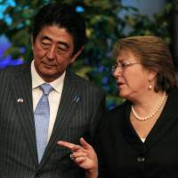 Prime Minister Shinzo Abe leans in to listen to Chilean President Michelle Bachelet as they wait for their staff to exchange folders, after each leader delivered a statement, at  the La Moneda presidential palace, in Santiago on Thursday. | AP