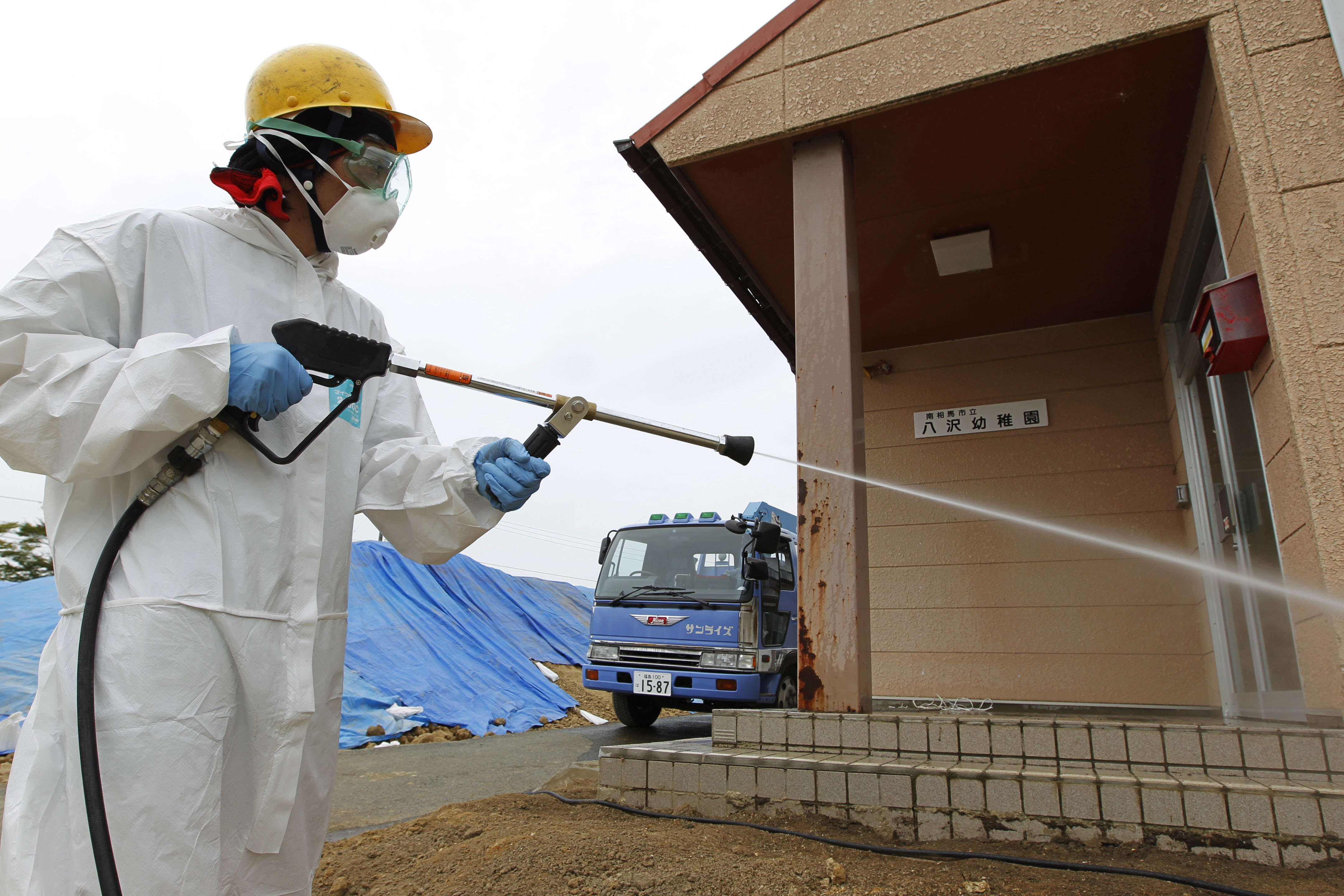 A worker uses a pressure hose in an attempt to wash radioactive particles off the exterior of a kindergarten in Minamisoma, about 20 km away from the severely damaged Fukushima No. 1 nuclear power plant, in August 2011. | AP