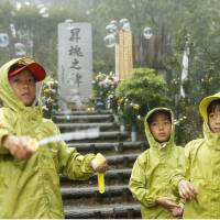 Children release bubbles Tuesday at a monument on Osutaka Ridge in Gunma Prefecture where JAL Flight 123 crashed. Mourners trekked there in heavy rain on the 29th anniversary of the accident. | KYODO