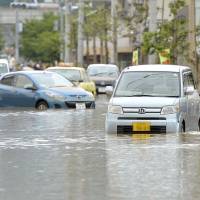 A driver wades through knee-deep water after getting out of his stranded car on a flooded road in Fukuchiyama, Kyoto Prefecture, at around noon on Sunday. In a 24-hour period that ended at 5:50 a.m. on Sunday, rainfall in the city surpassed 300 mm, submerging many roads and flooding many houses and businesses. | KYODO