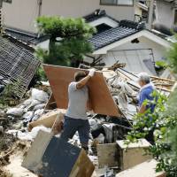 Residents remove debris in mudslide-hit Asaminami Ward, Hiroshima, on Tuesday. The death toll from the disaster has risen to 60, while rescuers continue the search for 26 people still missing. | KYODO