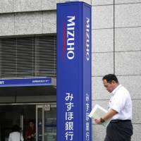 A man walks past a Mizuho Bank branch in Tokyo in May. Mizuho Financial Group will offer analysts the opportunity to switch jobs so their knowledge about industries and the equity market can be used to advise clients. | BLOOMBERG