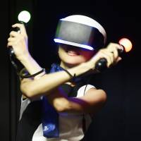 A model wearing Sony\'s Project Morpheus, a head-mounted display, shakes light sticks to play its PS4 video game console at the annual Tokyo Game Show at Makuhari Messe hall in the city of Chiba on Thursday. | KYODO