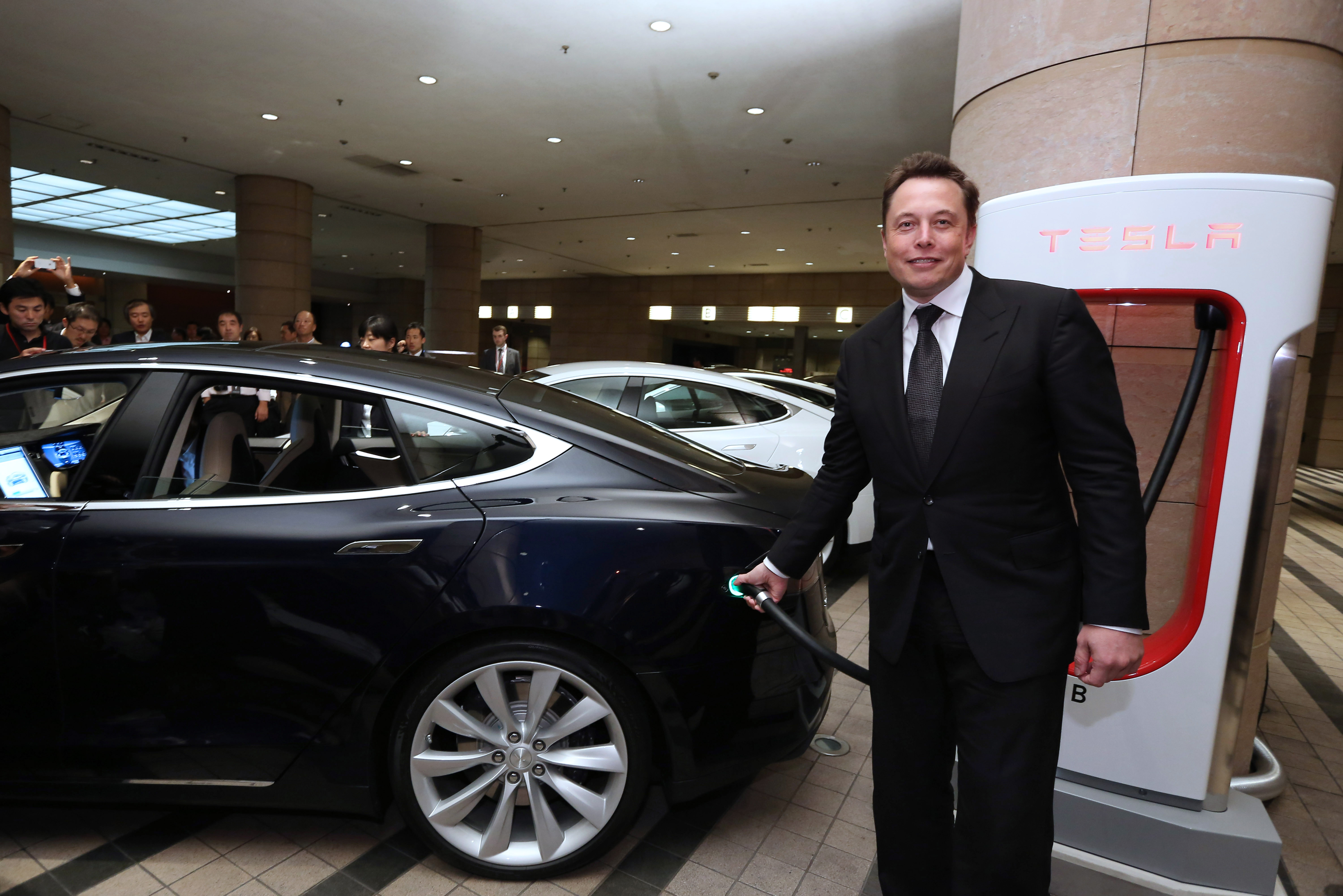 Elon Musk, co-founder and chief executive officer of Tesla Motors Inc., demonstrates how to charge the company's Model S electric sedan following a news conference in Tokyo on Monday. | BLOOMBERG
