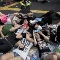 People look at their mobile phones as they lay on the ground at a pro-democracy demonstration occupying Nathan Road, a major route through the heart of the Kowloon district of Hong Kong, on Monday. | AFP-JIJI