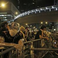 Wrapped in plastic to shield himself from pepper spray, a student protester stands behind a makeshift barrier blocking main streets in the central business district of Hong Kong on late Monday. | AP