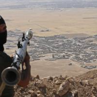 A Kurdish peshmerga fighter holds a rocket-propelled grenade launcher as he takes up position in an area overlooking the Iraqi village of Baretle (background), which is controlled by the Islamic State, on Monday in Khazir, on the edge of Mosul. | REUTERS
